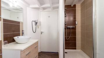 A modern bathroom with a white sink, a glass shower enclosure, and a door leading to another room.