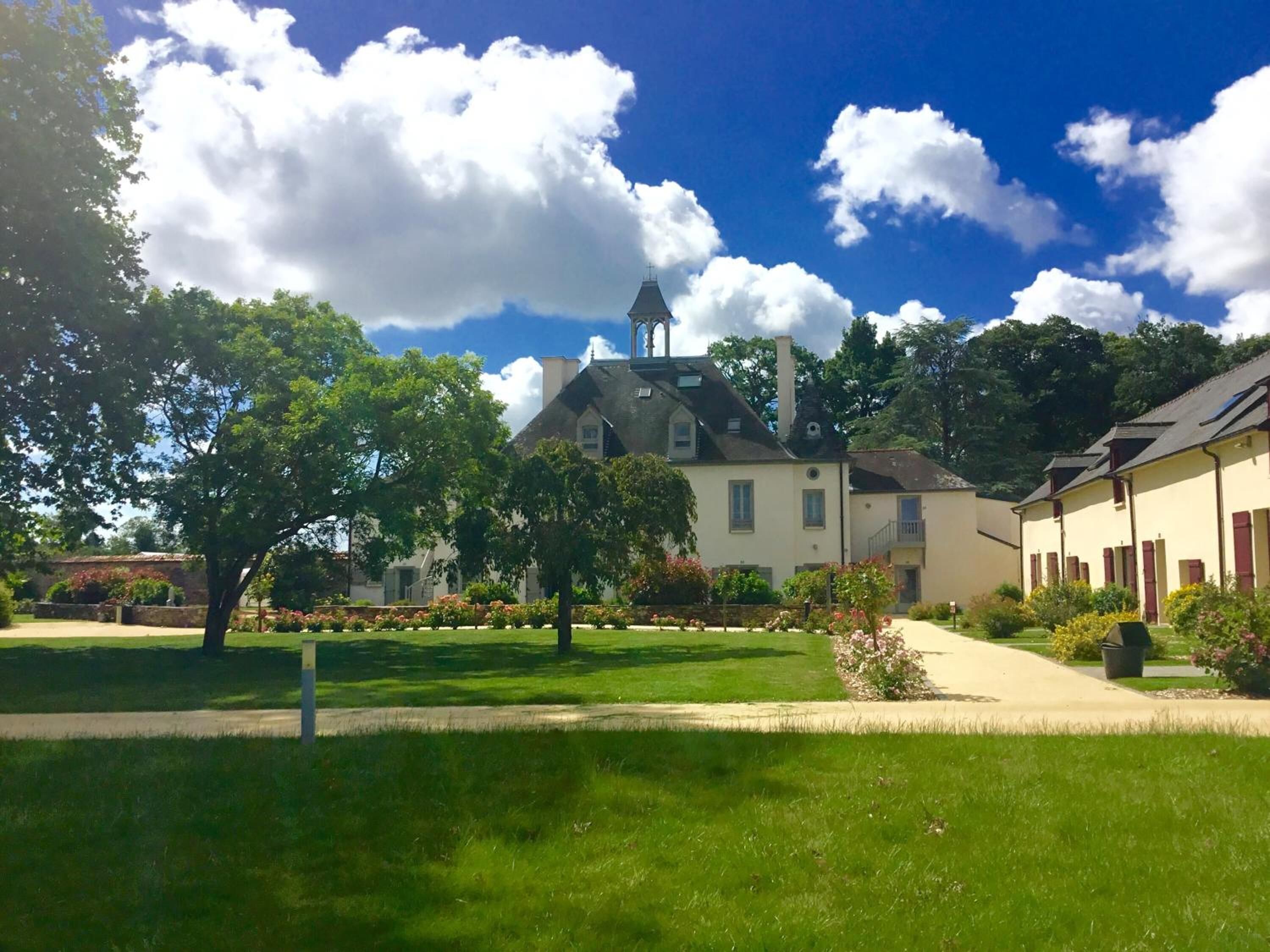 En innergård med en stor byggnad som har ett markant torn, omgiven av frodig grönska och en klarblå himmel.