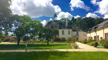 En innergård med en stor byggnad som har ett markant torn, omgiven av frodig grönska och en klarblå himmel.