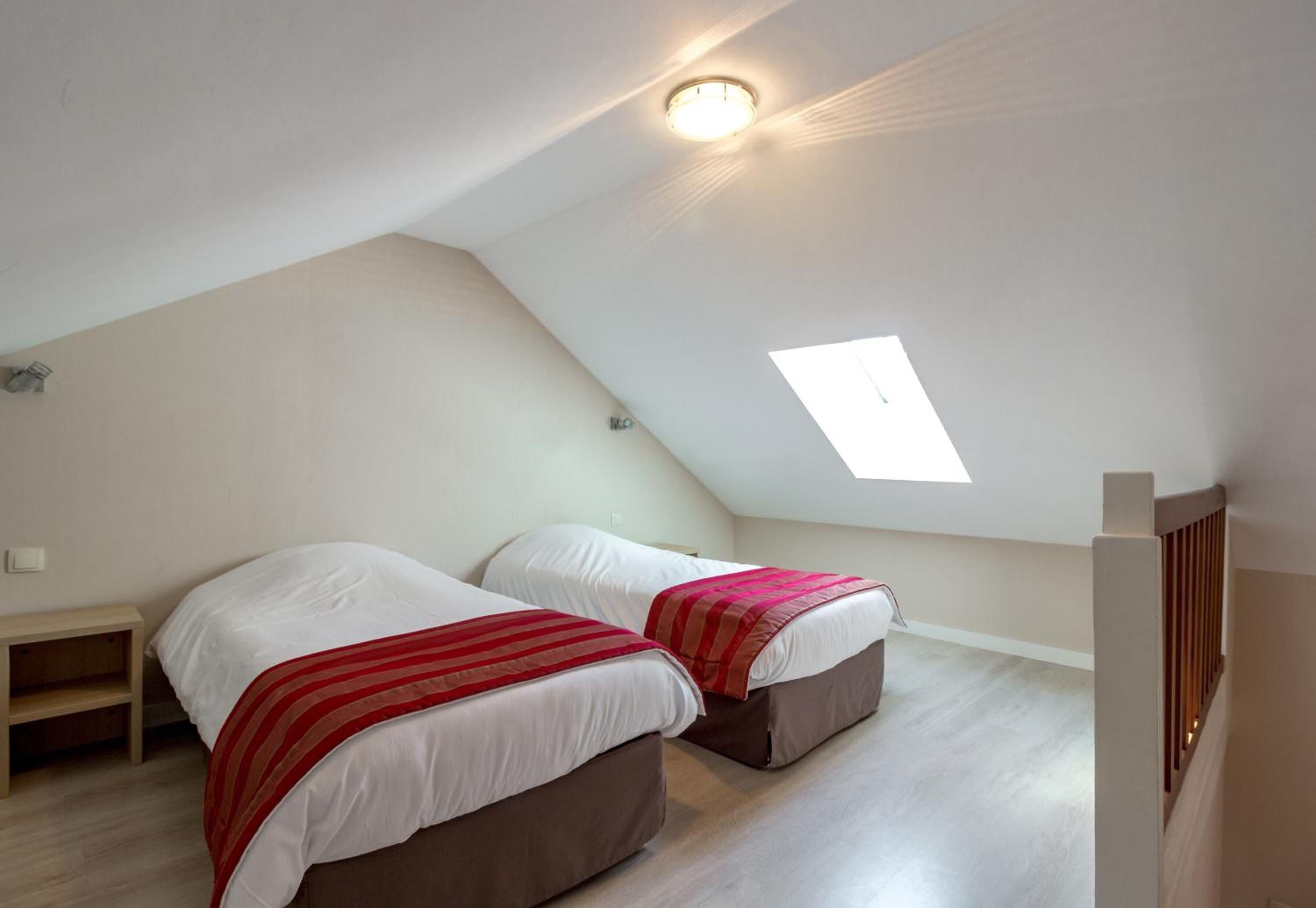 A small, triangular attic bedroom with two beds, a skylight, and a wooden nightstand.