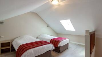 Un pequeño dormitorio en ático, de forma triangular, con dos camas, un tragaluz y una mesita de noche de madera.