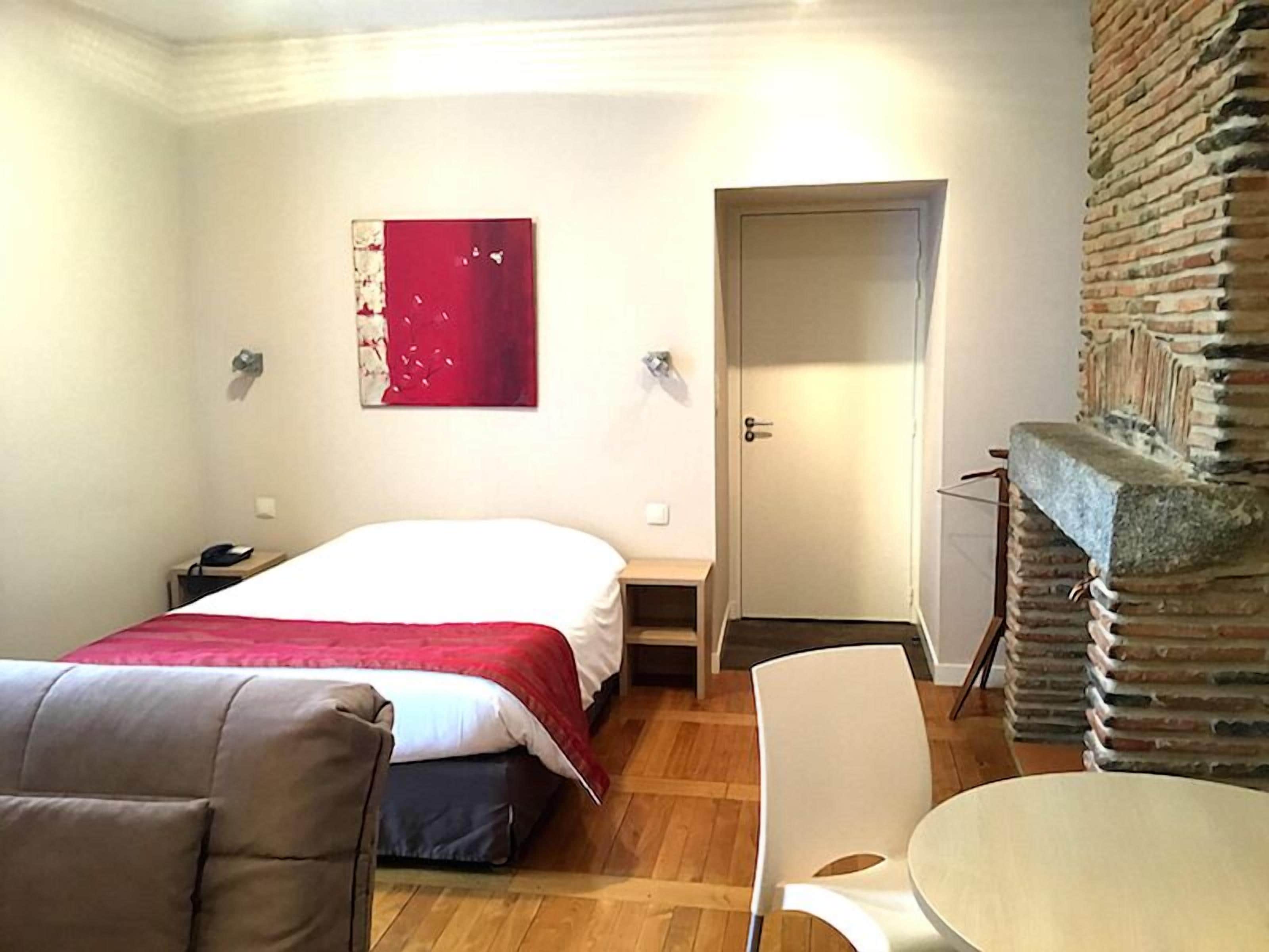 Una habitación de hotel con cama, una silla, una mesita pequeña, una obra de arte roja en la pared y una chimenea de piedra.