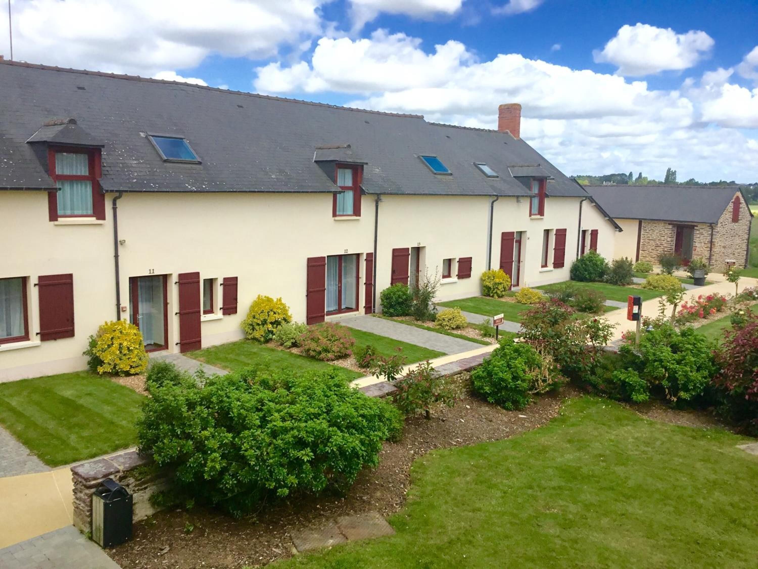 A row of two-story houses with dormer windows, a stone building, and well-maintained gardens.