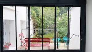 A sliding glass door leading to an outdoor patio area with a red bench, a blue table, and a green chair.