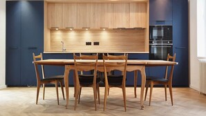 A modern kitchen with wooden cabinets, a built-in oven, and a dining area with a table and chairs.