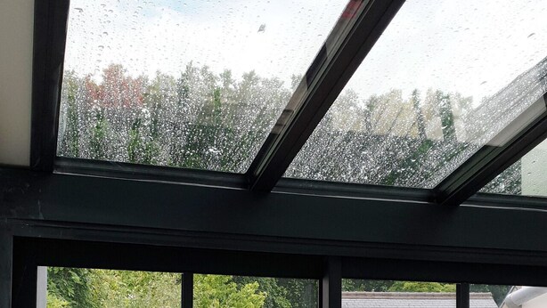 A view through a window with raindrops, a red bench, and a green chair outside.