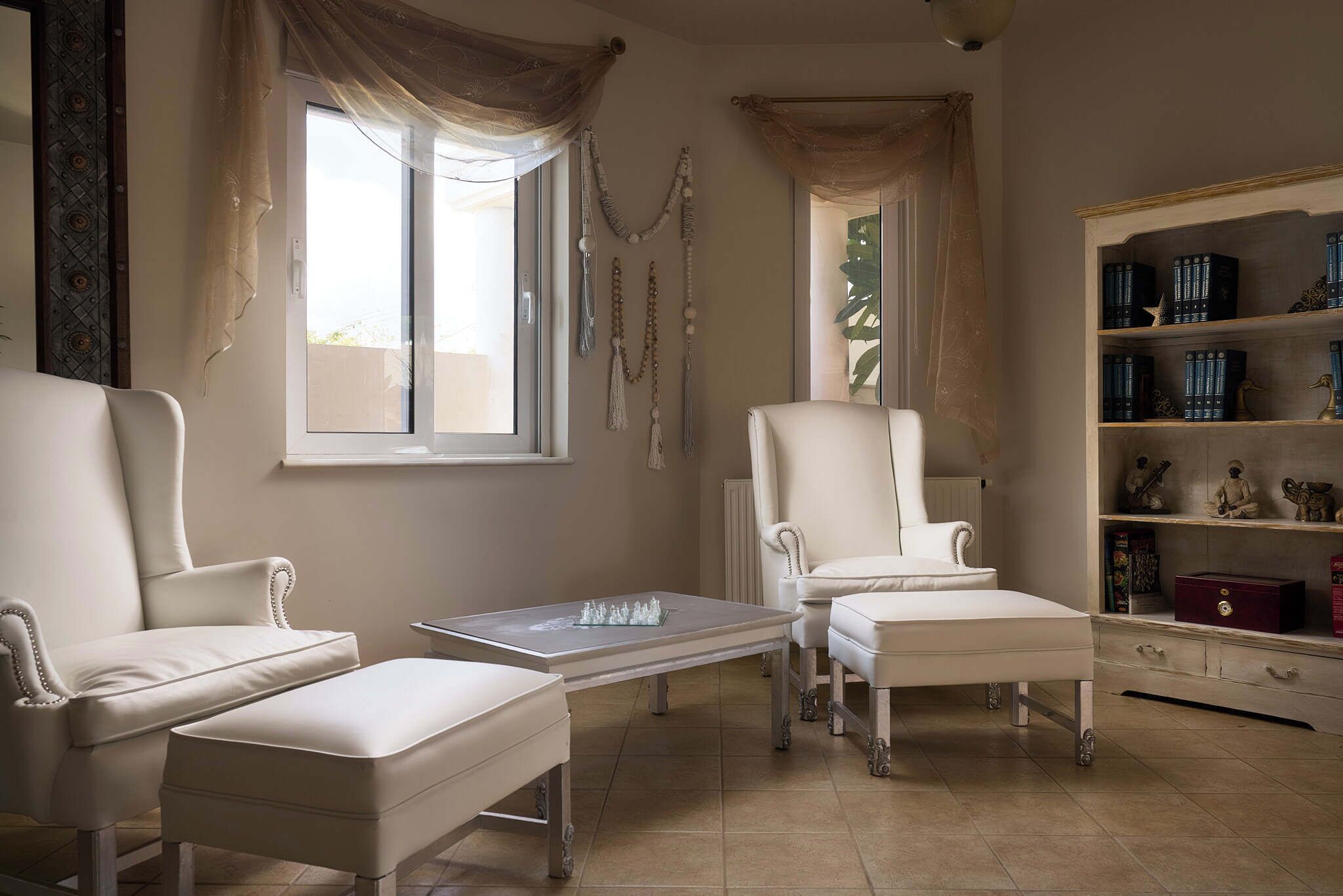 A room with two white armchairs, a small table, and a bookshelf with books and decorative items.
