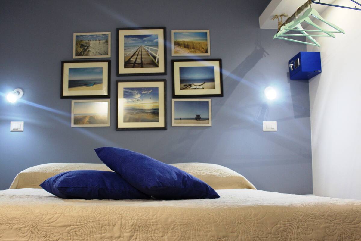 Ein Schlafzimmer mit einem Bett, einem blauen Kopfkissen und einer Wand mit gerahmten Bildern.
