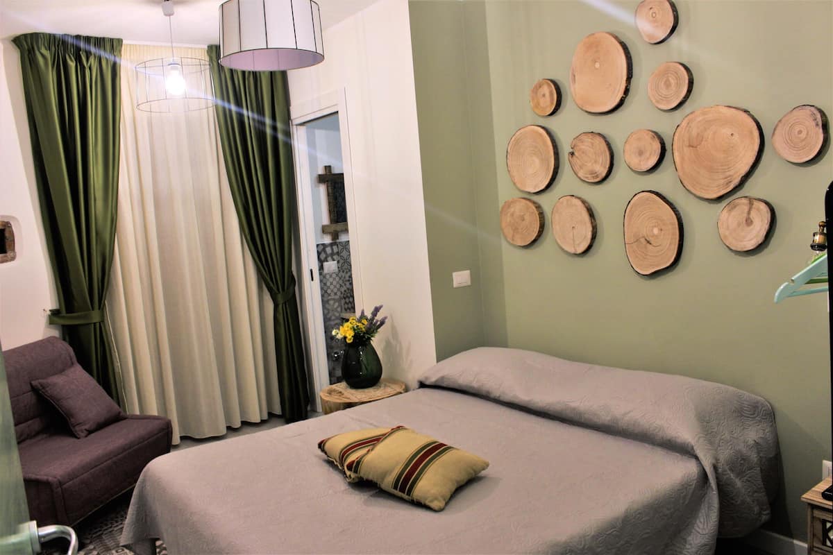 Ein Schlafzimmer mit Bett, einem Sessel, einer Vase mit Blumen und einer Wand mit Holzschnitten.