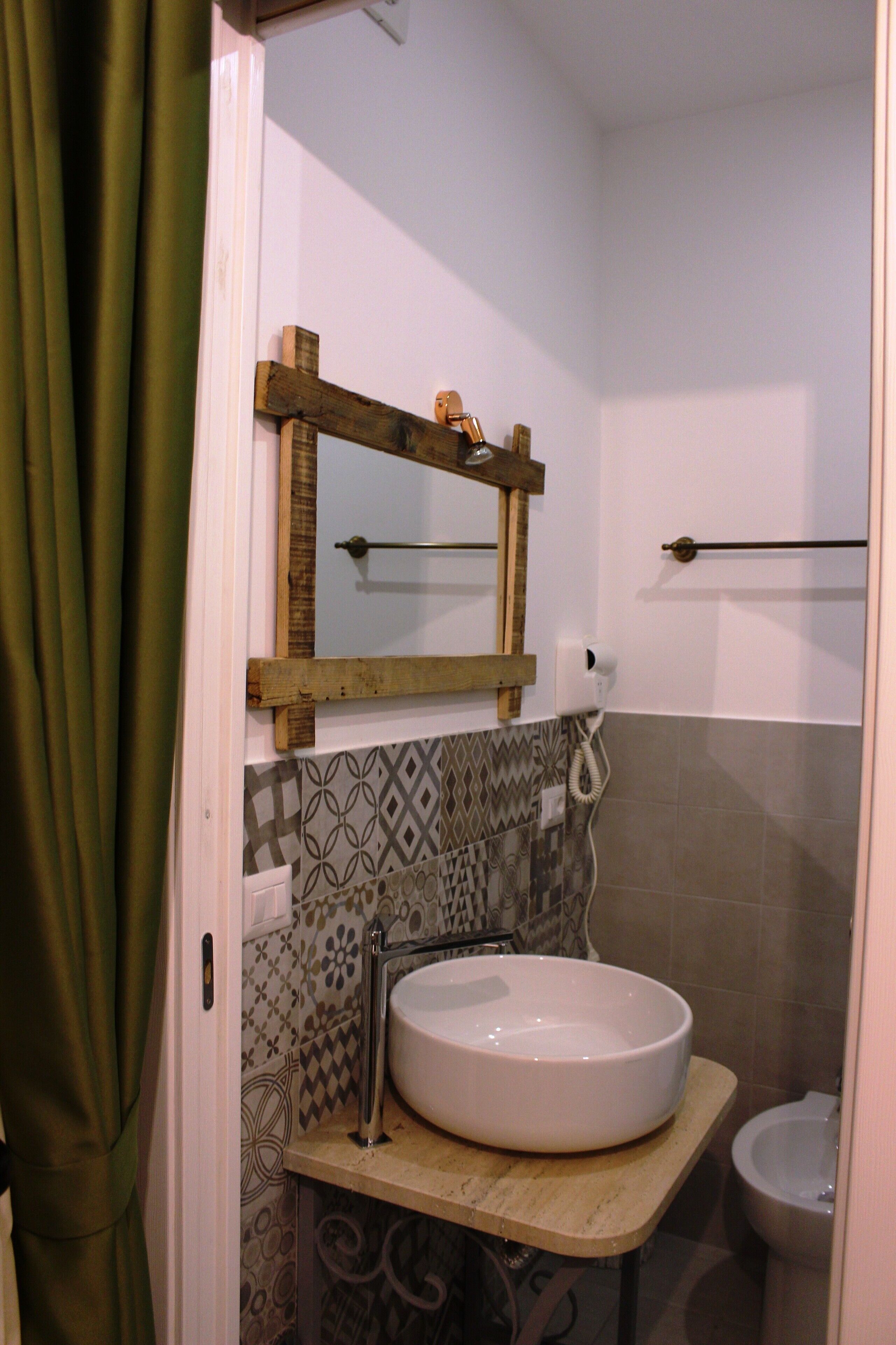 A bathroom with a large white sink, a wooden-framed mirror, patterned tiles, and a toilet.