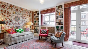 A cozy living room with a patterned wall, a red armchair, a grey armchair, a sofa, and a large window with curtains. - 3 Bedroom Apartment on Portobello Road in Notting Hill (London)