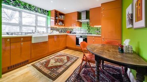 A modern kitchen with orange cabinets, a dining table, and a patterned rug. - 3 Bedroom Apartment on Portobello Road in Notting Hill (London)