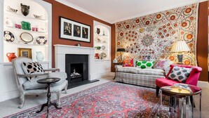 A living room with a fireplace, patterned rug, and a variety of decorative items on shelves and walls. - 3 Bedroom Apartment on Portobello Road in Notting Hill (London)