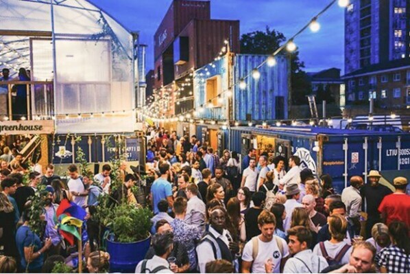 A crowded outdoor event with a greenhouse tent and people gathered around.