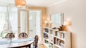 Un coin repas avec une table en bois, des chaises, un lustre, une bibliothèque et un miroir au mur.