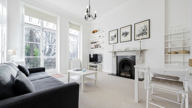 A modern living room with a black sofa, white coffee table, and a fireplace. There are bookshelves and a TV on the wall. - Elegant Earl's Court 2 bed 2 Bath Near Tube (London)