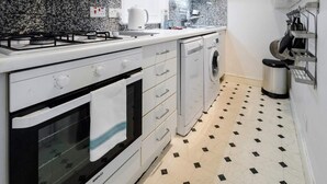 A compact kitchen with a gas stove, oven, washing machine, and a microwave. - Elegant Earl's Court 2 bed 2 Bath Near Tube (London)