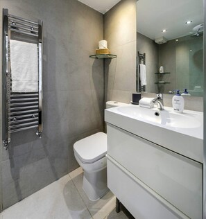 A modern bathroom with a glass shower enclosure, a white toilet, and a vanity with a mirror. - Elegant Earl's Court 2 bed 2 Bath Near Tube (London)
