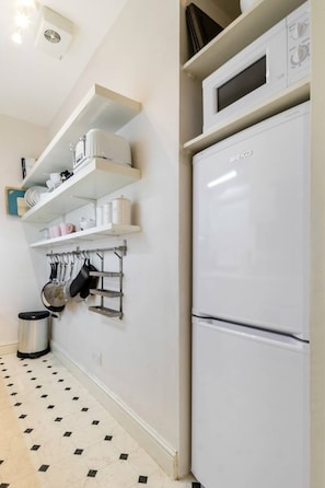 Kitchen area with a refrigerator, shelving units, and kitchenware.
