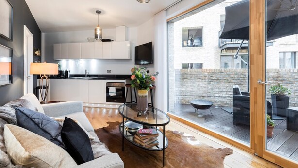 Un salon moderne avec un canapé, une table basse et une vue sur un balcon aménagé avec du mobilier d’extérieur.