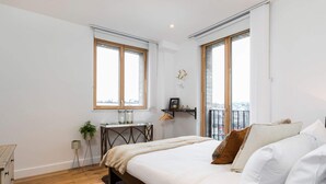 Une chambre avec un grand lit, un petit bureau et deux fenêtres.