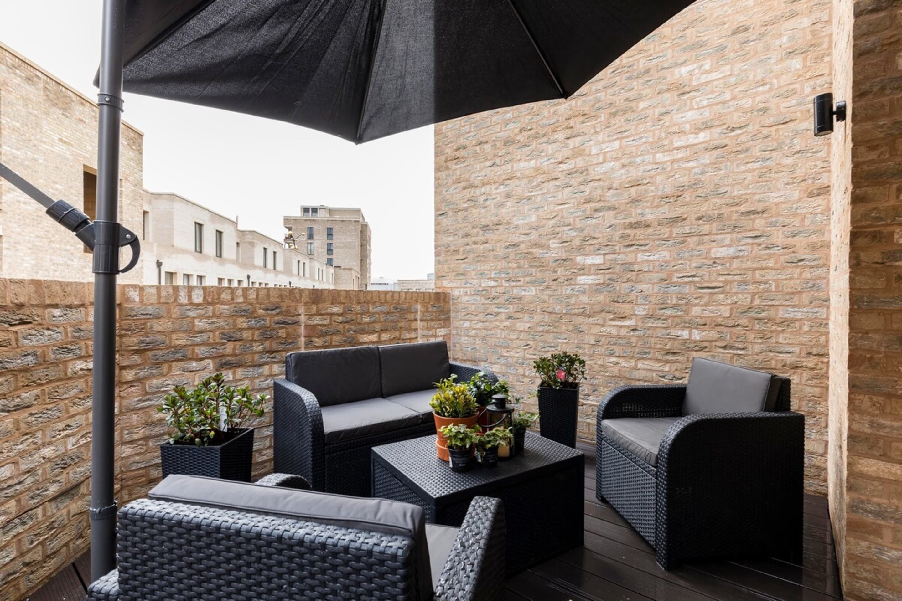 Een terras met rieten meubels, potplanten en een zwarte parasol.