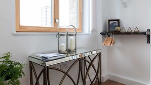 Une pièce avec une fenêtre à cadre en bois, une table en verre ornée de bougies, une tête de cerf fixée au mur et une étagère sur laquelle sont disposés des objets décoratifs.