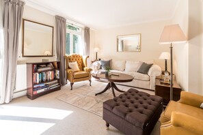 A well-lit living room with a sofa, armchair, ottoman, and a bookshelf.