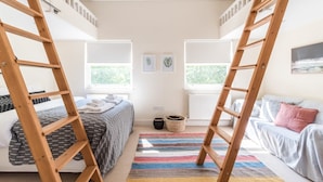 A bedroom with bunk beds, a bed with a patterned blanket, a colorful rug, and a window with blinds.