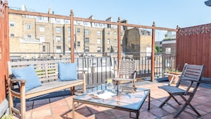 A terrace with a wooden bench, a glass table, and two chairs.