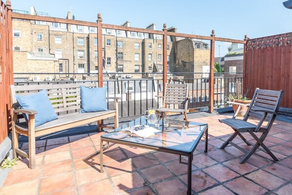 A terrace with a wooden bench, a glass table, and two chairs.