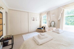 A bedroom with a large bed, a chair, a vanity with a mirror, and a window with curtains.