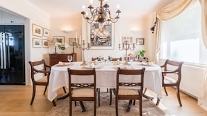 A dining room with a chandelier, a table set for six, and a large painting on the wall.