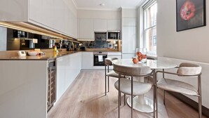 A modern kitchen with white cabinetry, a central island, and a round dining table with chairs. - Lovely 2 Bed near Covent Garden & Tube (London)