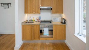 A compact kitchen with wooden cabinets, a stainless steel stove, a microwave, and a window providing natural light.