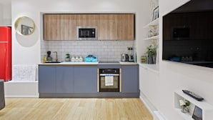 A modern kitchen with grey cabinets, a wooden upper section, a built-in microwave, and a small oven. - Trendy 1 Bedroom Apartment in the Heart of London (London)