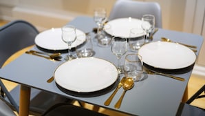A dining table set with white plates, gold cutlery, and clear glasses. - Trendy 1 Bedroom Apartment in the Heart of London (London)