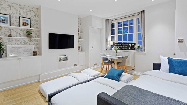 A modern hotel room with two beds, a desk, and a window with a view of a bridge. - Trendy 1 Bedroom Apartment in the Heart of London (London)