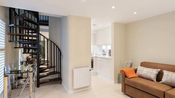 A modern living room with a brown sofa, a glass dining table, and a spiral staircase leading to an upper level. - Bright 1 Bedroom House near Edgware Road (London)
