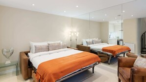 A modern hotel room with two beds, a glass bedside table, a brown leather armchair, and a large mirror. - Bright 1 Bedroom House near Edgware Road (London)
