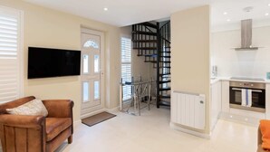 A modern living room with a flat-screen TV, a brown leather sofa, and a staircase leading to a kitchen area. - Bright 1 Bedroom House near Edgware Road (London)