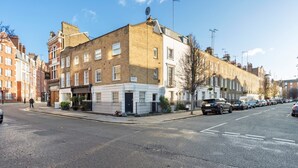 A street view with a row of terraced houses, parked cars, and a clear sky. - Bright 1 Bedroom House near Edgware Road (London)