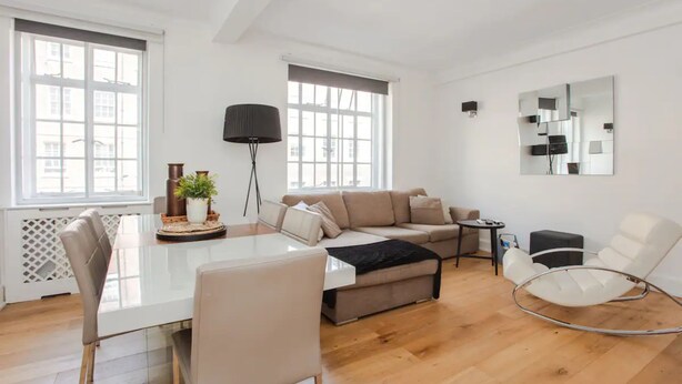 A modern living room with a glass dining table, a beige sofa, a white armchair, and a black floor lamp. - Modern 2 Bedroom Apartment in Marble Arch (London)
