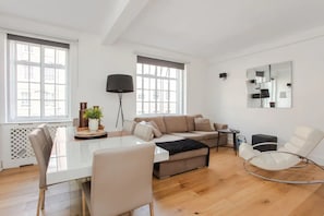 A modern living room with a glass dining table, a beige sofa, a white armchair, and a black floor lamp. - Modern 2 Bedroom Apartment in Marble Arch (London)