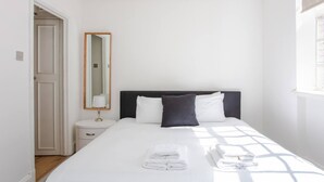 A hotel room with a bed, a bedside table, a mirror, and a window. - Modern 2 Bedroom Apartment in Marble Arch (London)