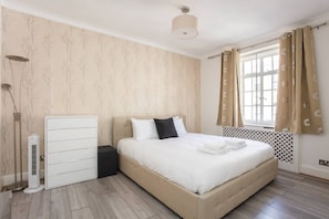 A bedroom with a bed, a radiator, a wardrobe, and a window with curtains. - Modern 2 Bedroom Apartment in Marble Arch (London)