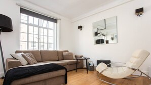 A modern living room with a sofa, a rocking chair, a small table, and a large window. - Modern 2 Bedroom Apartment in Marble Arch (London)