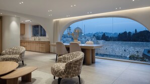 A modern living room with a dining area, large arched windows, and a view of a historic cityscape. - Western Wall View Apartment (Jerusalem)