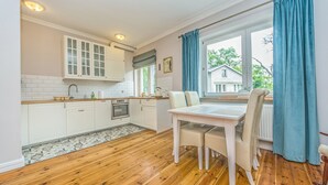 A kitchen with white cabinets, a wooden floor, and a dining table with chairs. - Victus Apartament Dębowa (Sopot)