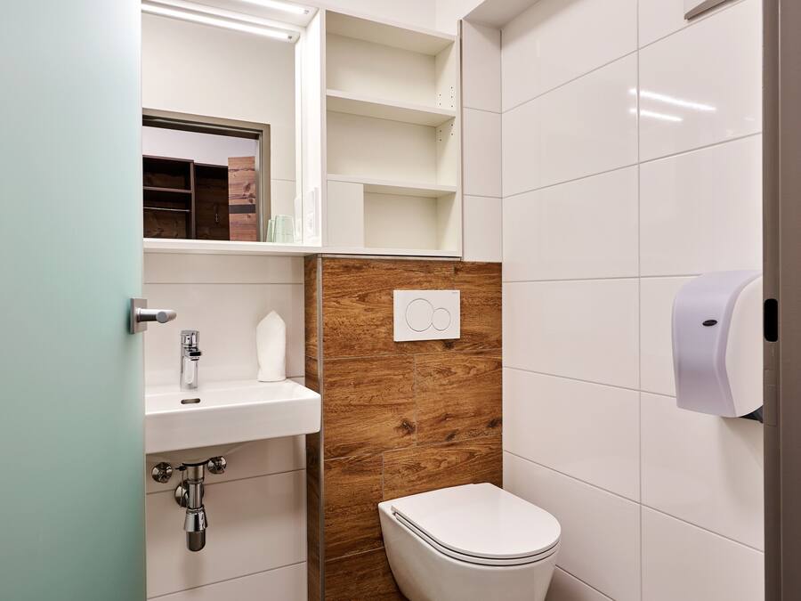 A modern bathroom with a white sink, wooden panel wall, white toilet, and a hand dryer.